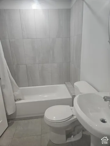 Bathroom featuring a white tub, pedestal sink, and toilet, complemented by light grey wall and floor tiling
