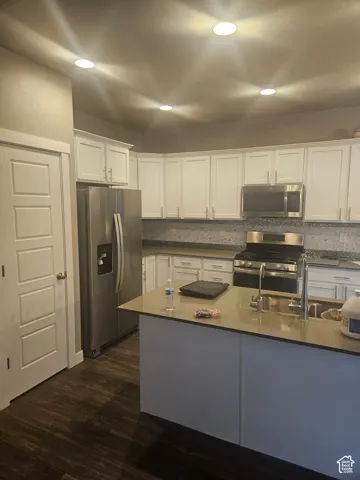 Kitchen featuring white cabinetry, stainless steel appliances, a center island with sink, mosaic tile backsplash, and wood-finish flooring