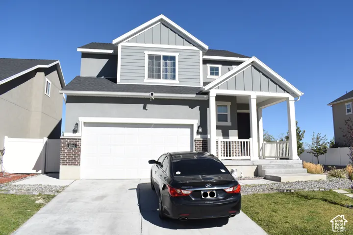 Two-story residence with a covered front porch featuring white columns and railing, a two-car garage, and gray siding accents
