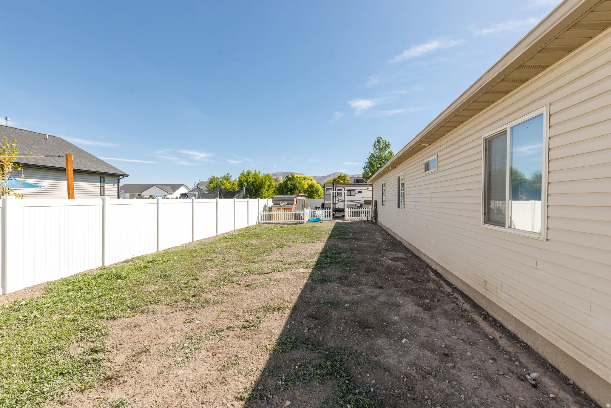Vinyl siding exterior with multiple windows, a white vinyl fence, and a partially grassed yard