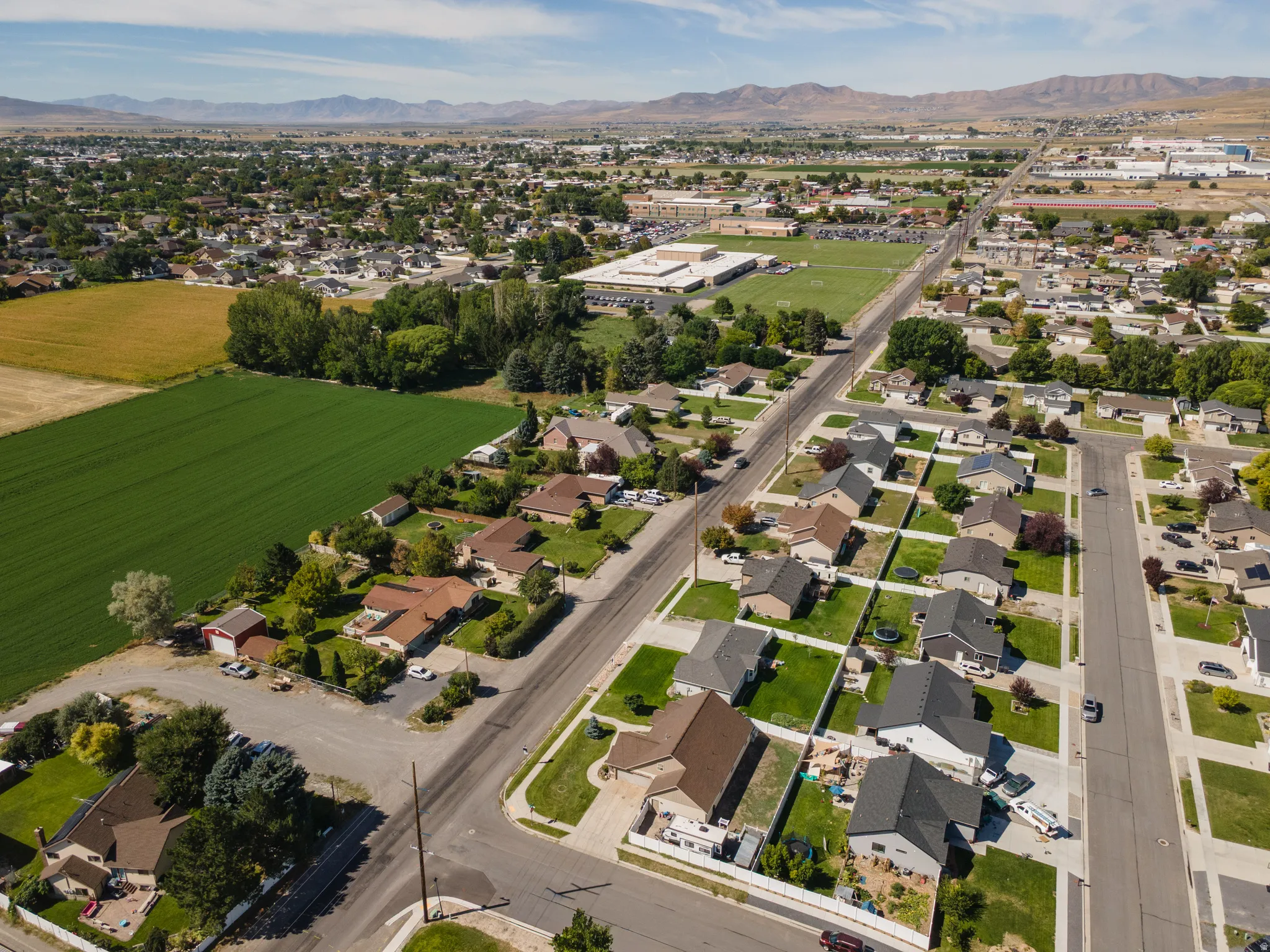Residential street with single-family homes, surrounding green fields, and distant mountains