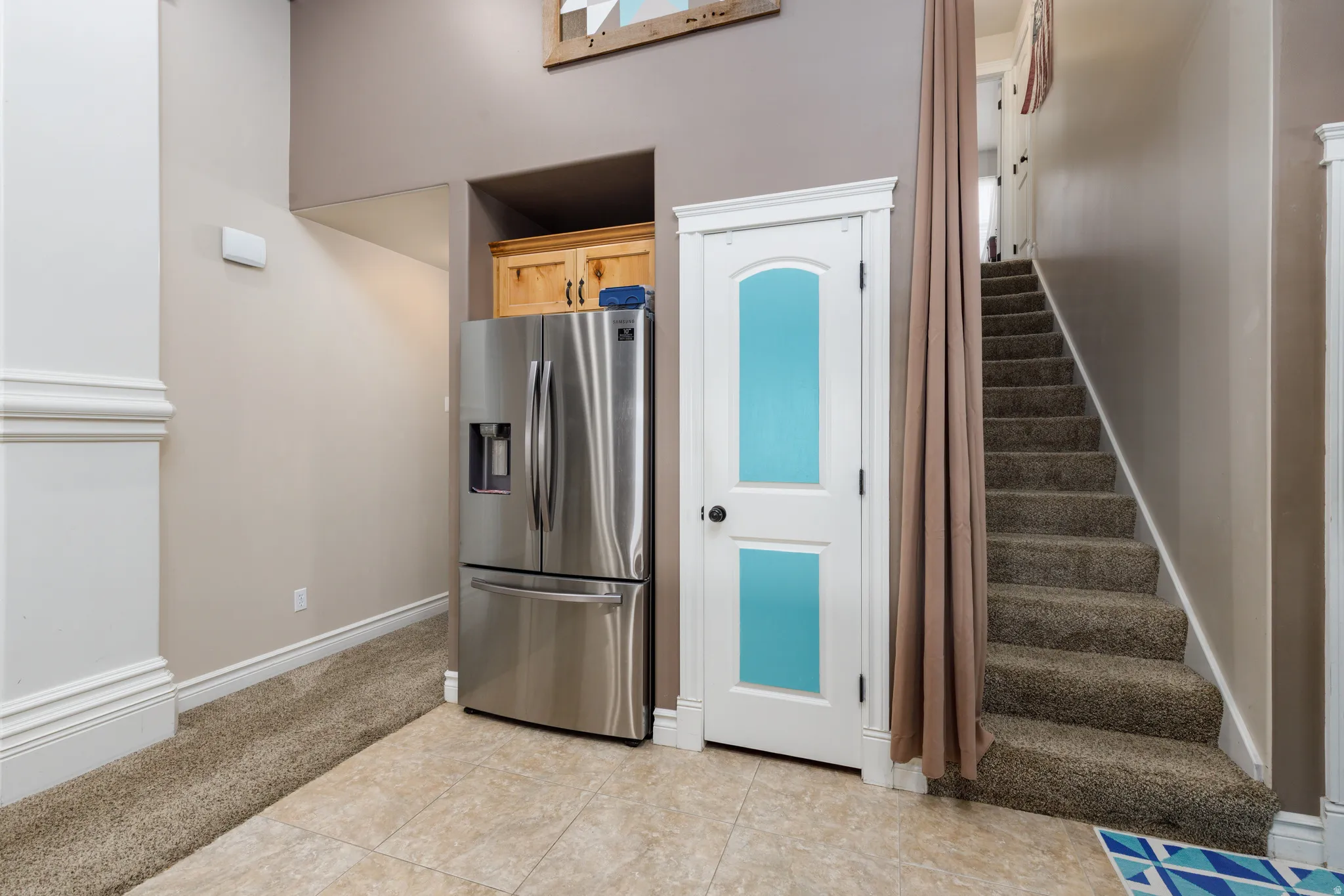 Stainless steel refrigerator, built-in wooden cabinetry, white paneled door with frosted glass inserts, and carpeted staircase
