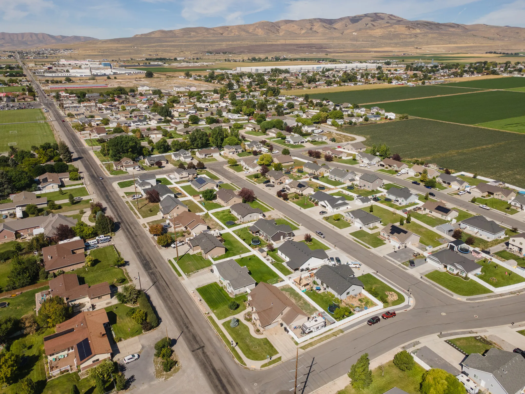Residential neighborhood with established streets and sidewalks, surrounded by agricultural fields and distant mountains