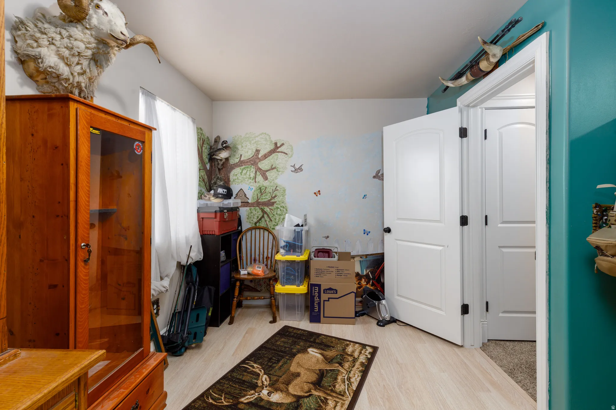 Light-toned wood-finish flooring, white paneled doors with dark hardware, and a wall featuring a painted mural