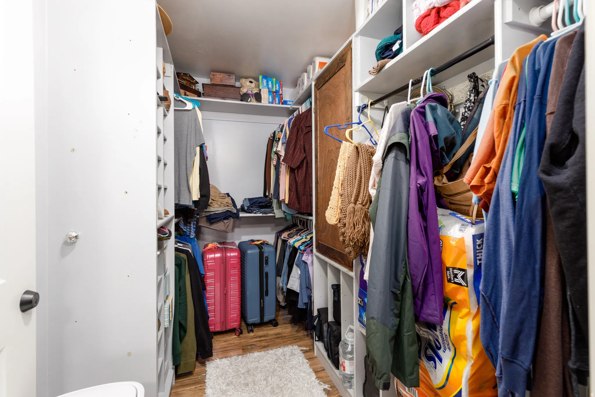 Walk-in closet featuring wood-finish flooring, white shelving, and hanging rods