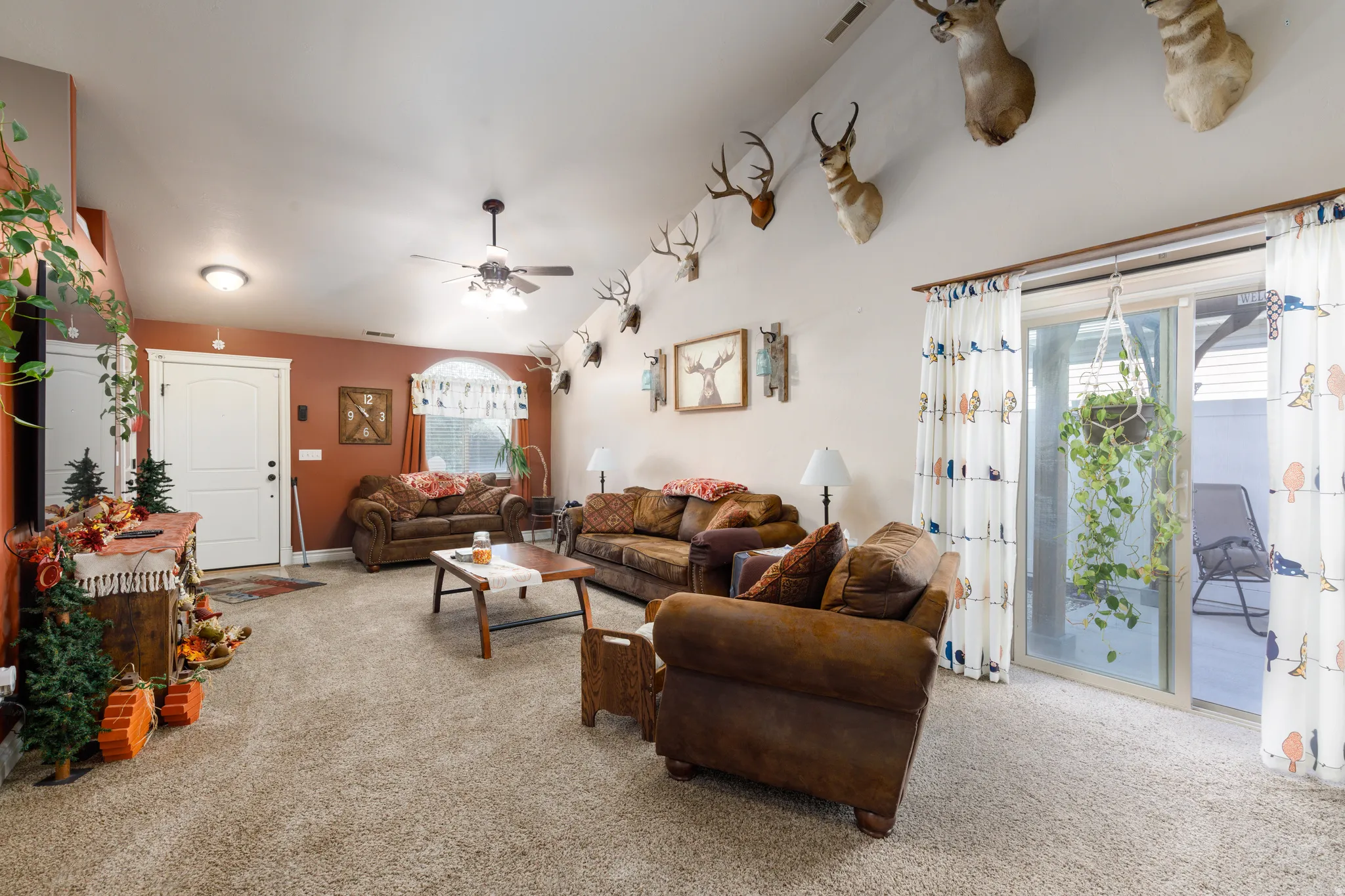 Vaulted ceiling with an integrated ceiling fan, carpet flooring, and a sliding glass door to the exterior