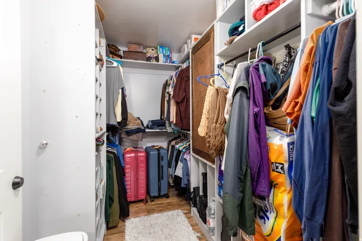 Walk-in closet featuring wood-finish flooring, white shelving, and hanging rods