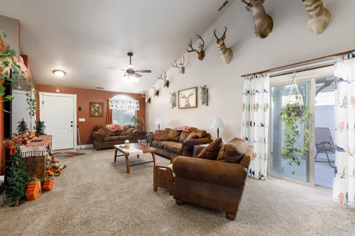 Vaulted ceiling with an integrated ceiling fan, carpet flooring, and a sliding glass door to the exterior