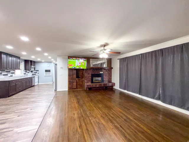 Hardwood flooring, brick fireplace with mantel, dark wood cabinetry, recessed lighting, and a ceiling fan