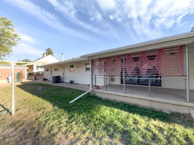 Expansive backyard featuring a covered patio with chain-link fencing, a dedicated concrete area, and an accessory structure