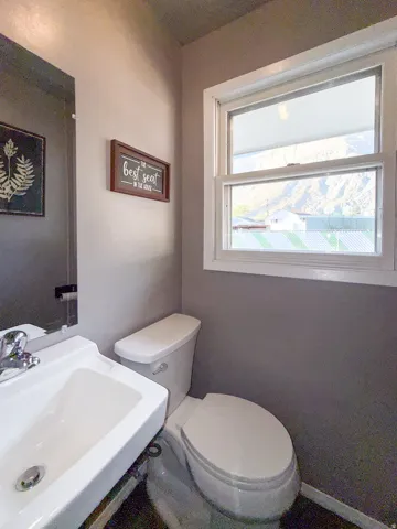 White pedestal sink with chrome faucet, standard toilet, and a window with mountain scenery