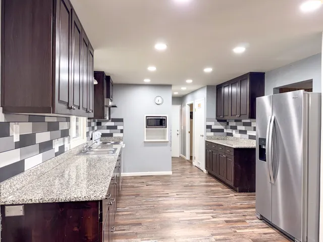 Kitchen featuring dark wood-finish cabinetry, light-toned countertops, a mosaic tile backsplash, wood-finish flooring, and recessed lighting