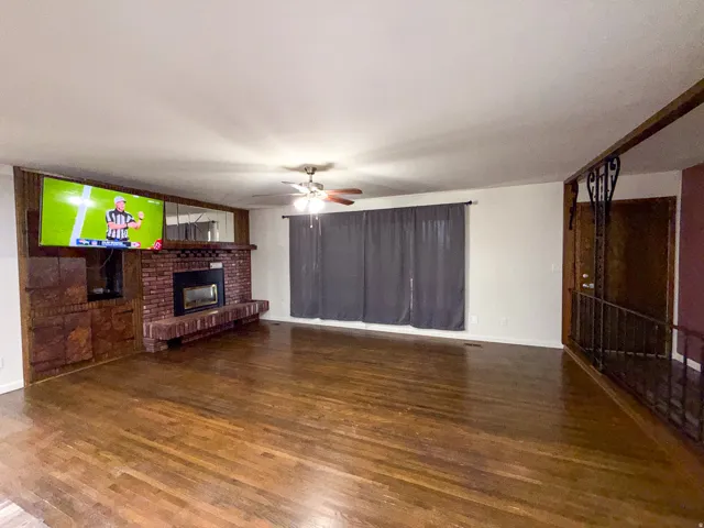 Brick fireplace with an integrated hearth, wood-finish flooring, and a ceiling fan