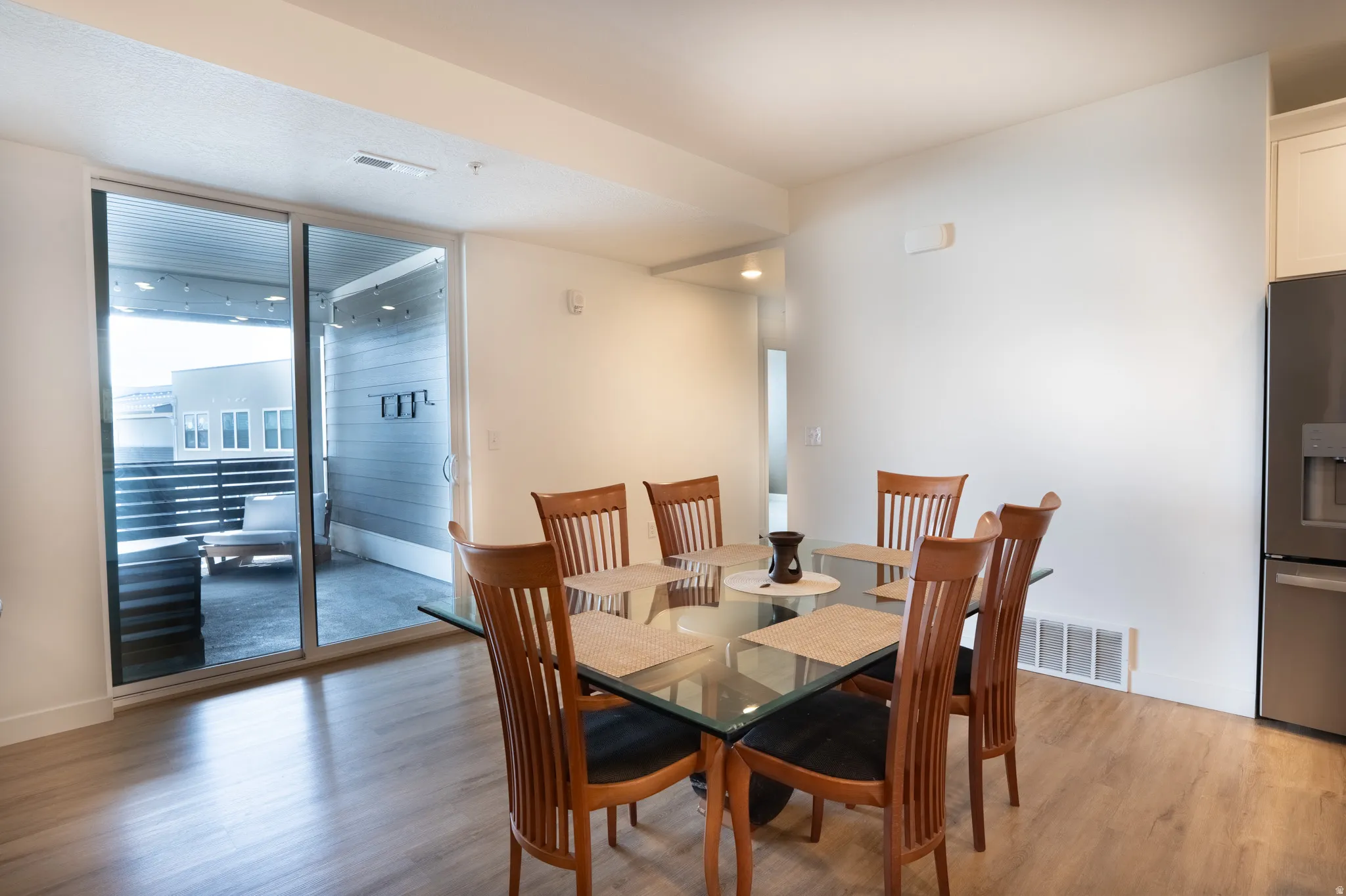 Wood-finish flooring, sliding glass patio door, integrated stainless steel refrigerator, white cabinetry, and recessed lighting
