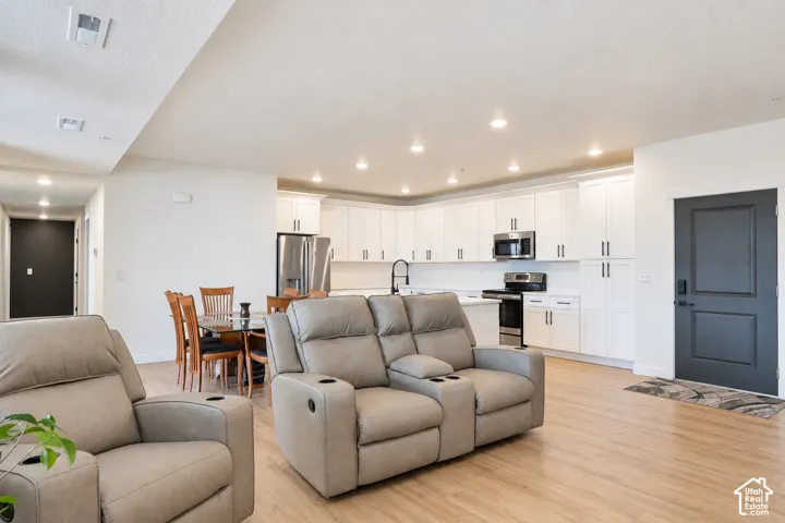 Open-concept living space featuring wood-finish flooring, recessed lighting, and a modern kitchen with white cabinetry and stainless steel appliances