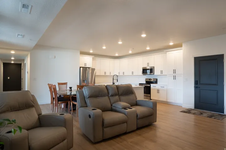 Open-concept living area featuring wood-finish flooring, recessed lighting, white cabinetry, stainless steel appliances, and a dark front door