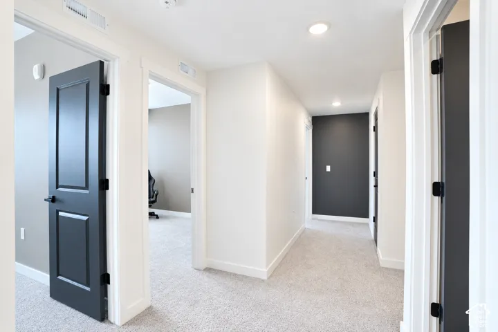 Hallway featuring recessed lighting, light-toned carpeting, white trim, and contrasting dark paneled doors with matte black hardware