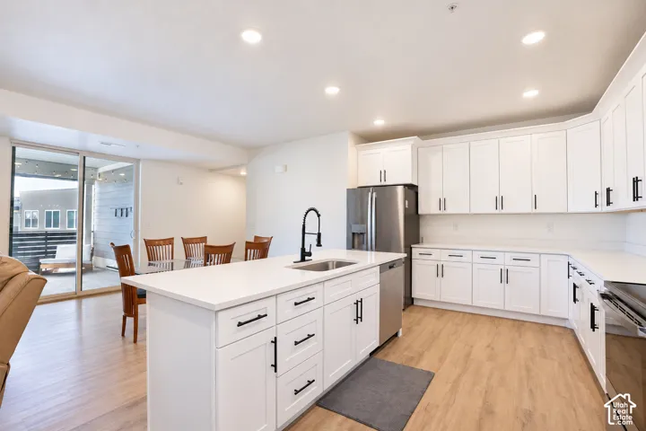Modern kitchen featuring white cabinetry with matte black hardware, stainless steel appliances, and a central island with a sink