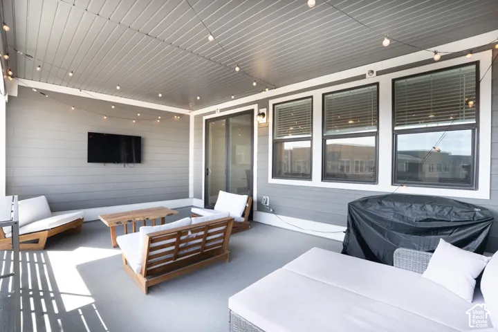 Covered outdoor patio featuring a slatted ceiling, string lighting, and a wall-mounted display
