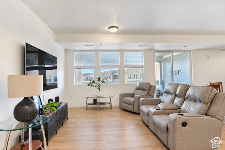 Recessed ceiling lighting, wood-finish flooring, multiple windows with horizontal blinds, and a sliding glass door to an exterior space