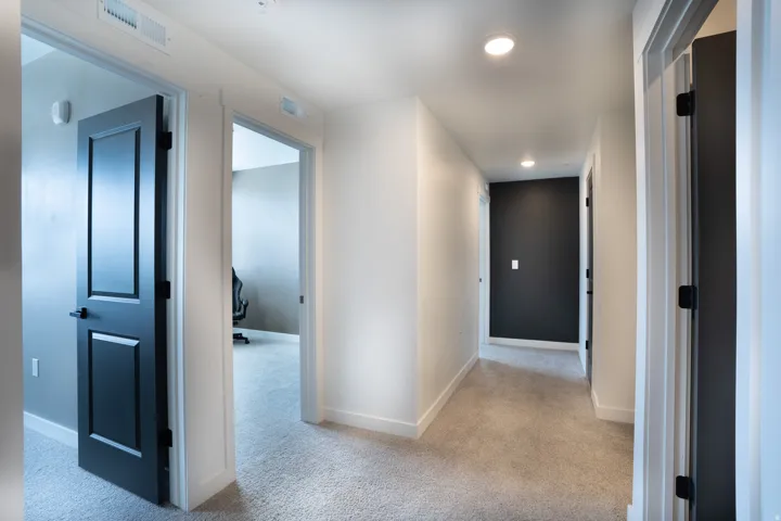 Hallway with recessed lighting, neutral carpet, white walls, black accent wall, and paneled doors with matte black hardware