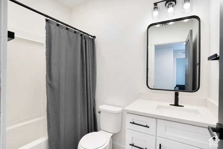 White vanity with integrated sink and matte black faucet, wall-mounted rectangular mirror with black frame, three-light vanity fixture, white toilet, and shower with white surround