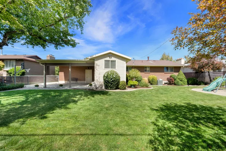 Expansive backyard featuring a manicured lawn, established perimeter landscaping, and a covered patio area