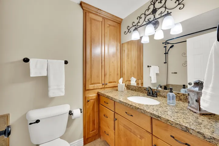 Vanity with an integrated sink, granite countertop, wood-finish cabinetry, and decorative wall-mounted lighting