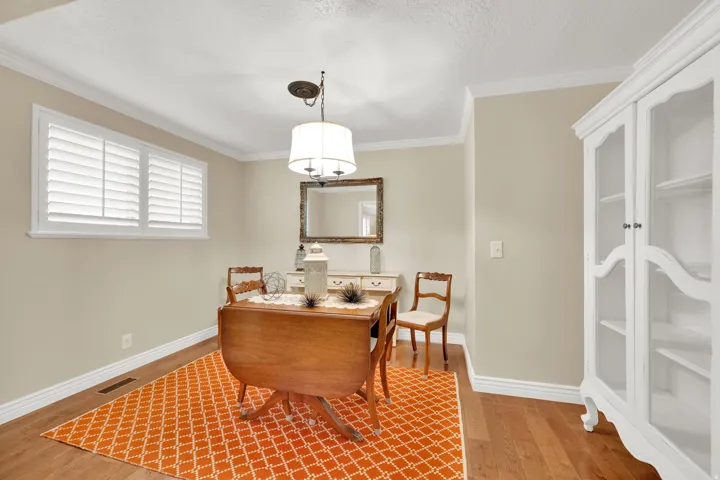 Hardwood flooring with crown molding, a built-in display cabinet, and a window with plantation shutters