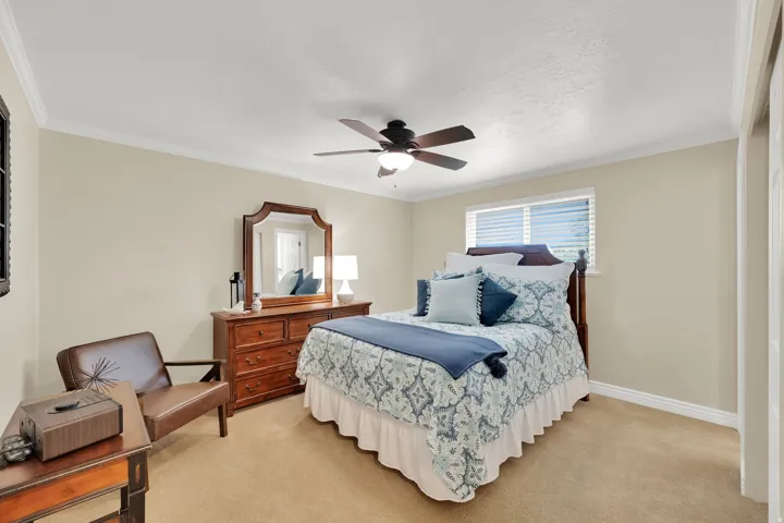 Neutral tone wall paint, crown molding, ceiling fan with integrated lighting, window with blinds, and carpeted flooring