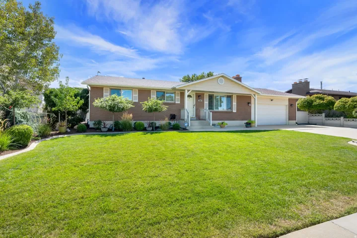 Brick and siding exterior with a covered entry, attached garage, concrete driveway, and a manicured lawn with mature landscaping