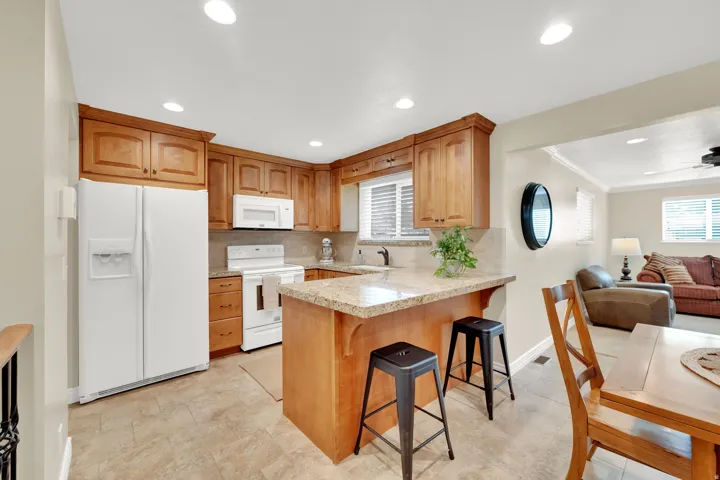 Kitchen featuring wood cabinetry, white appliances, a counter-height island with a stone-finish countertop, and tile flooring