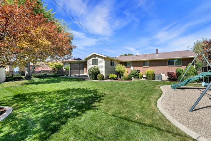 Expansive backyard featuring a manicured lawn, mature trees, a screened-in porch, and a brick and siding exterior