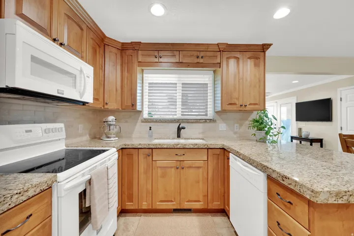 Kitchen featuring wood cabinetry, light-toned countertops, a white built-in microwave, white electric range, and a white dishwasher