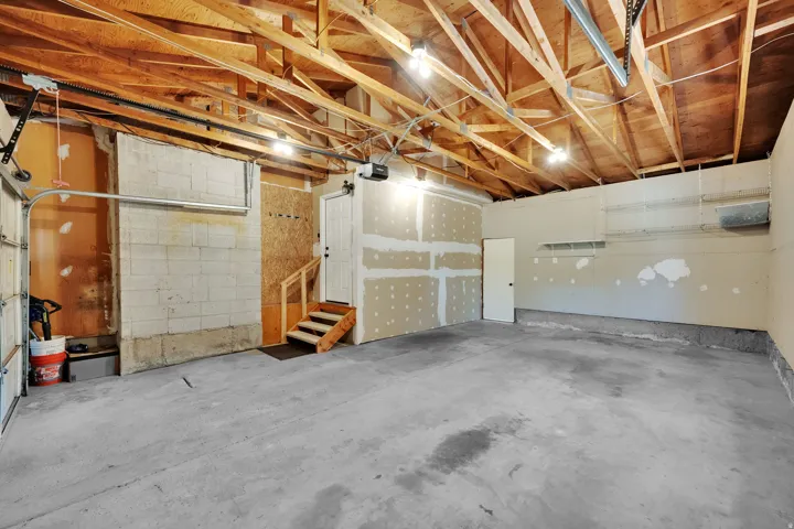 Concrete flooring, exposed wood beam ceiling, interior access door, wood stairs, overhead lighting