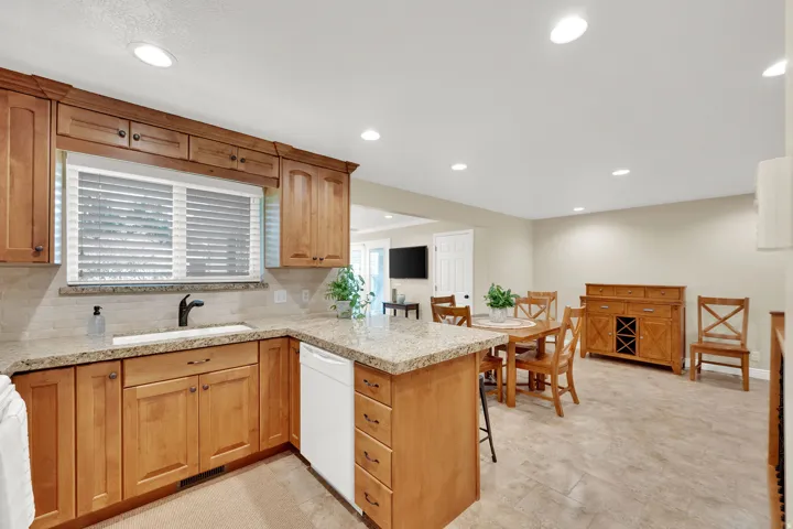 Kitchen with wood-finish cabinetry, light granite countertops, white tile backsplash, and a black-finish faucet