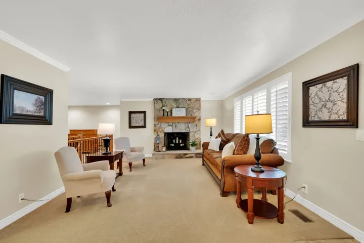 Stone-clad fireplace with wood mantel, white crown molding, shuttered windows, and neutral carpeting