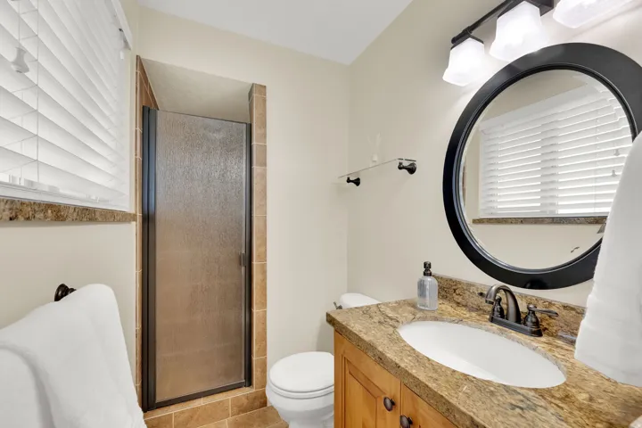 Enclosed shower with framed frosted glass door, tile flooring, wood-finish vanity with stone countertop, undermount sink, and dark bronze fixtures
