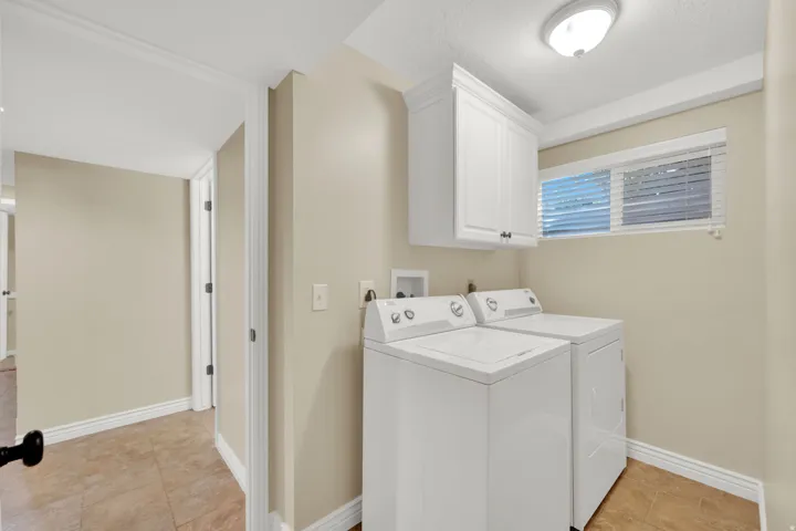 Laundry area featuring tiled flooring, a built-in upper cabinet, and a window with blinds