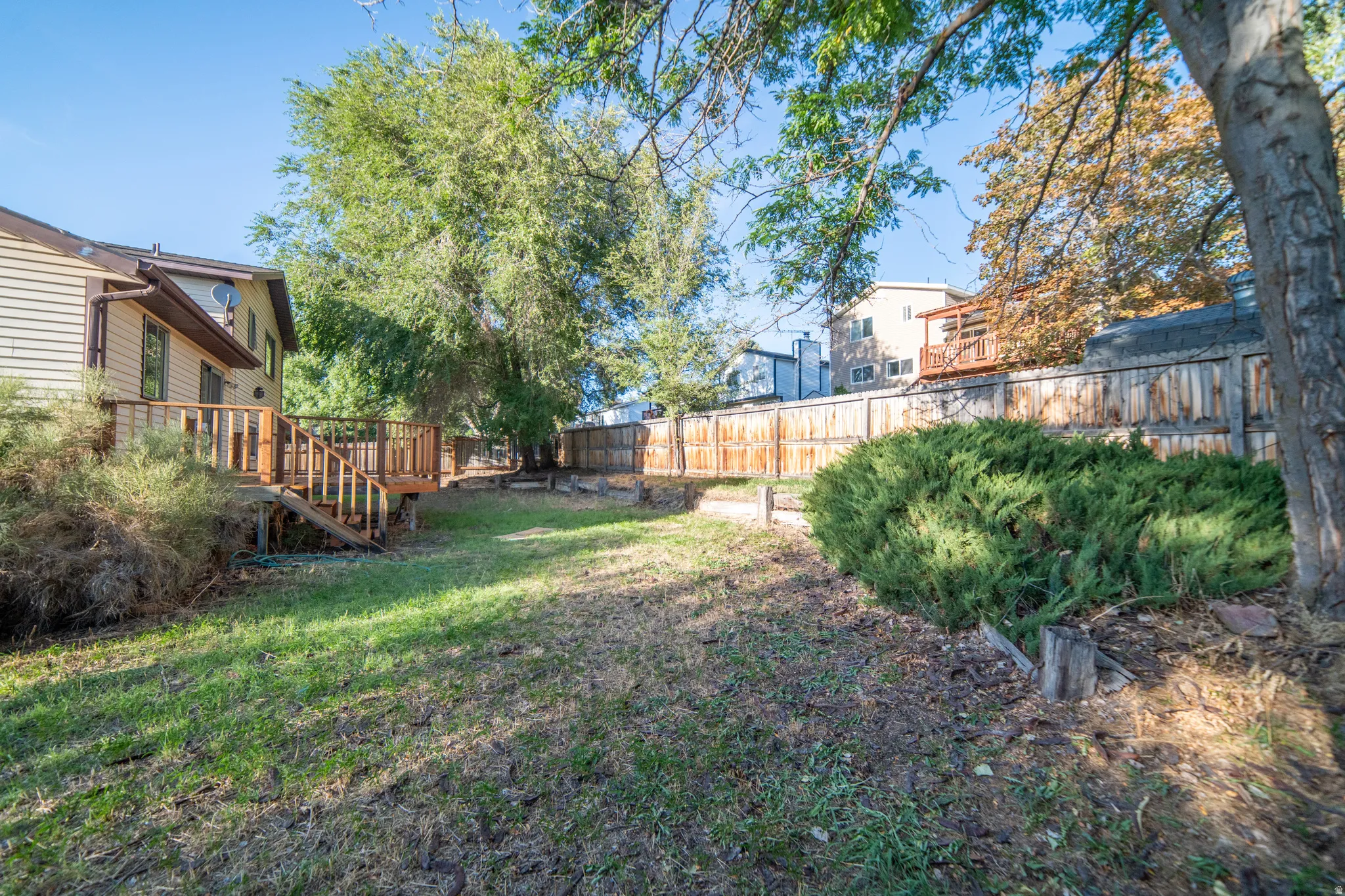 Expansive yard with wood fencing, mature trees, and a multi-level wood deck