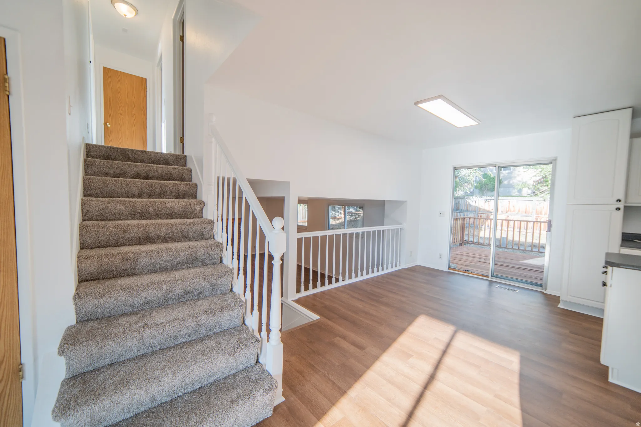 Carpeted staircase with white balusters, wood-finish flooring, white cabinetry, and sliding glass doors to outdoor decking