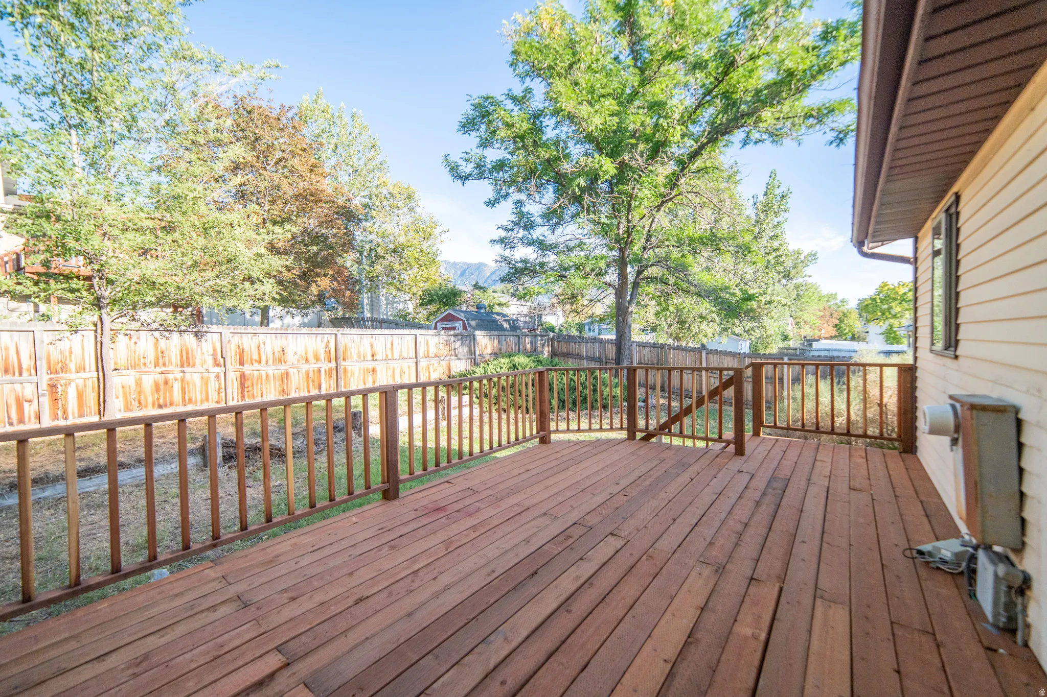 Expansive wood deck with a wood railing, offering a fenced backyard and mature trees