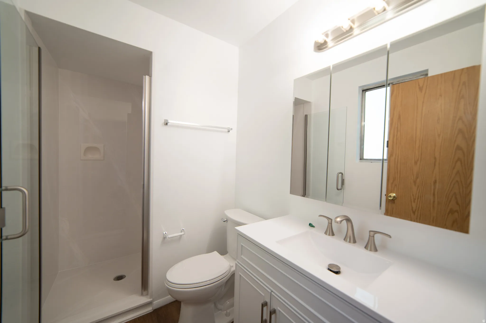 White vanity with integrated sink, brushed nickel faucet, large mirrored medicine cabinet, and glass-enclosed shower with white surround