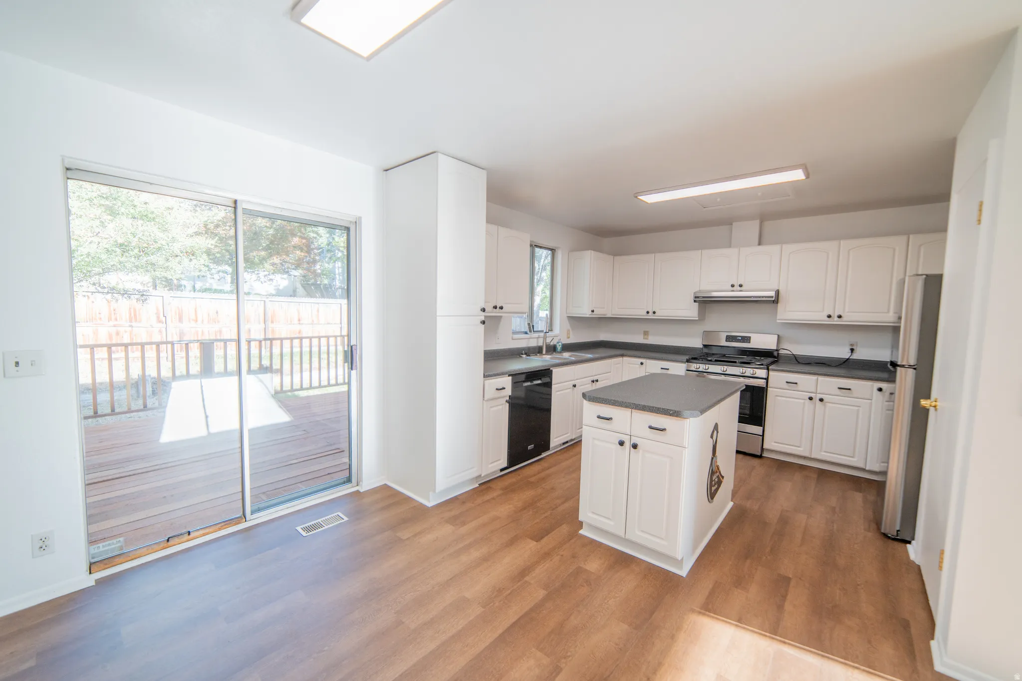 Kitchen featuring wood-finish flooring, white cabinetry, dark countertops, and stainless steel appliances