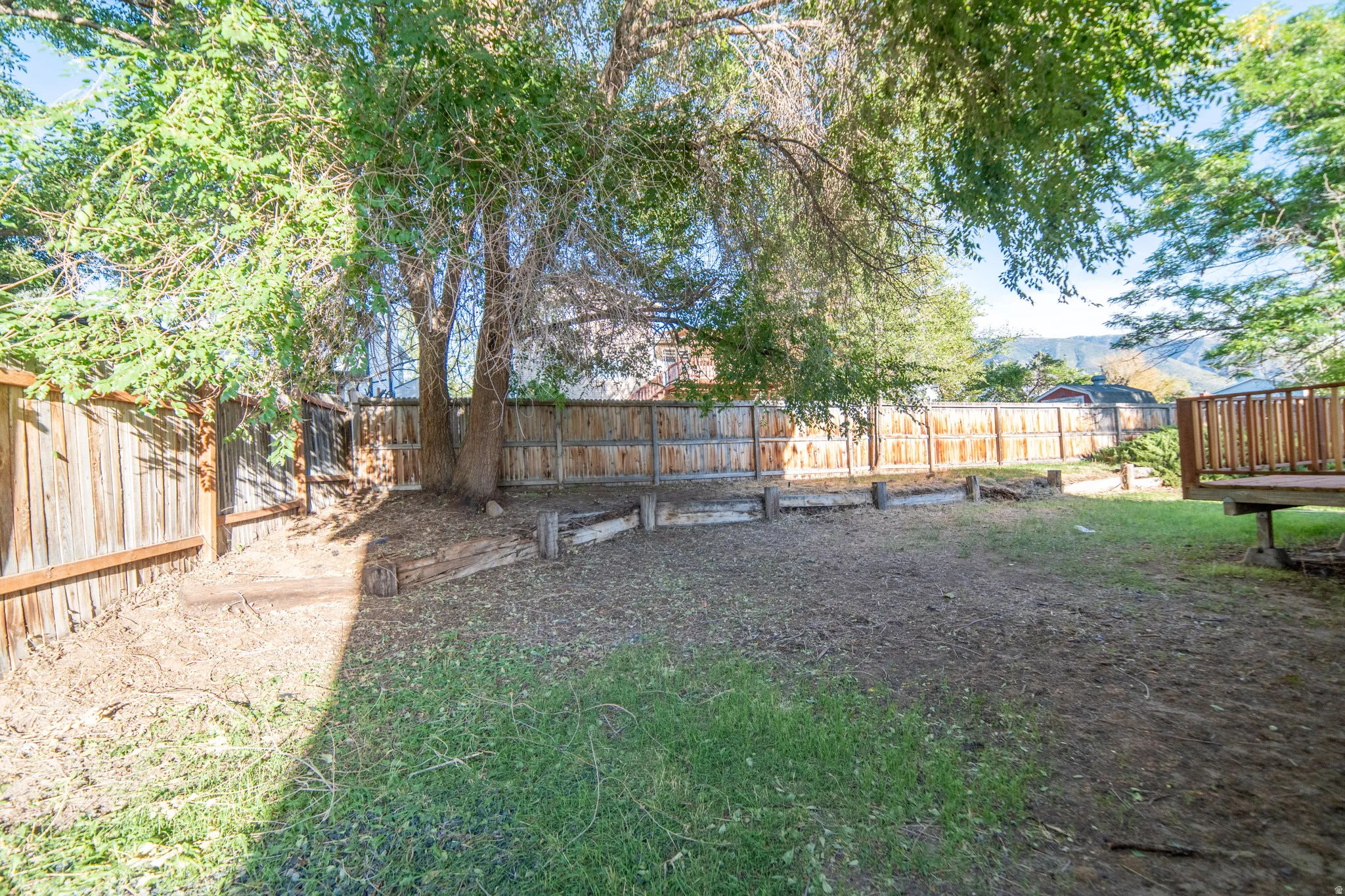 Expansive backyard featuring mature trees, wood fencing, a raised wood deck, and a tiered planter area