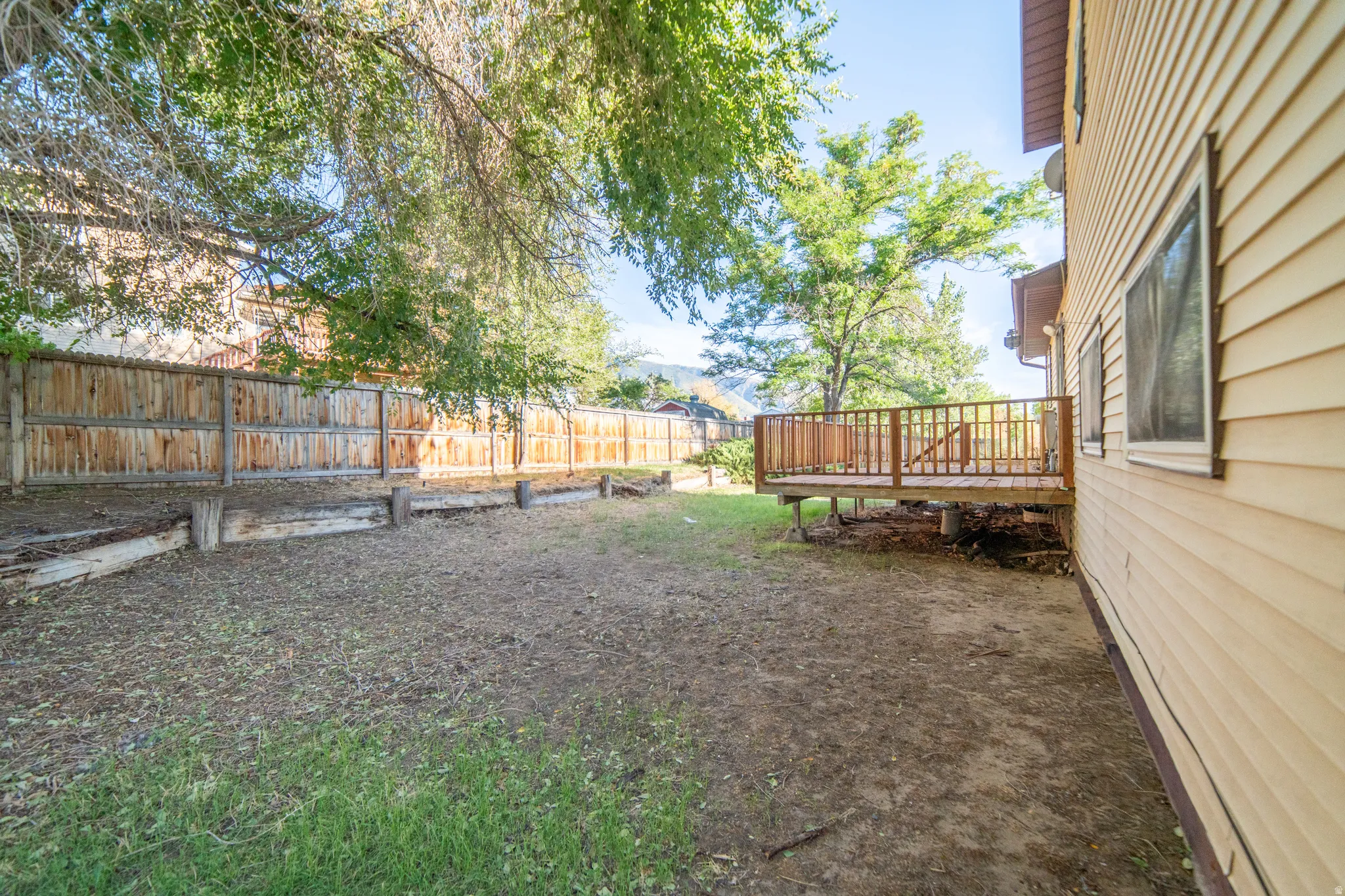 Expansive yard with wood fencing, a raised wood deck, and a wood-sided exterior