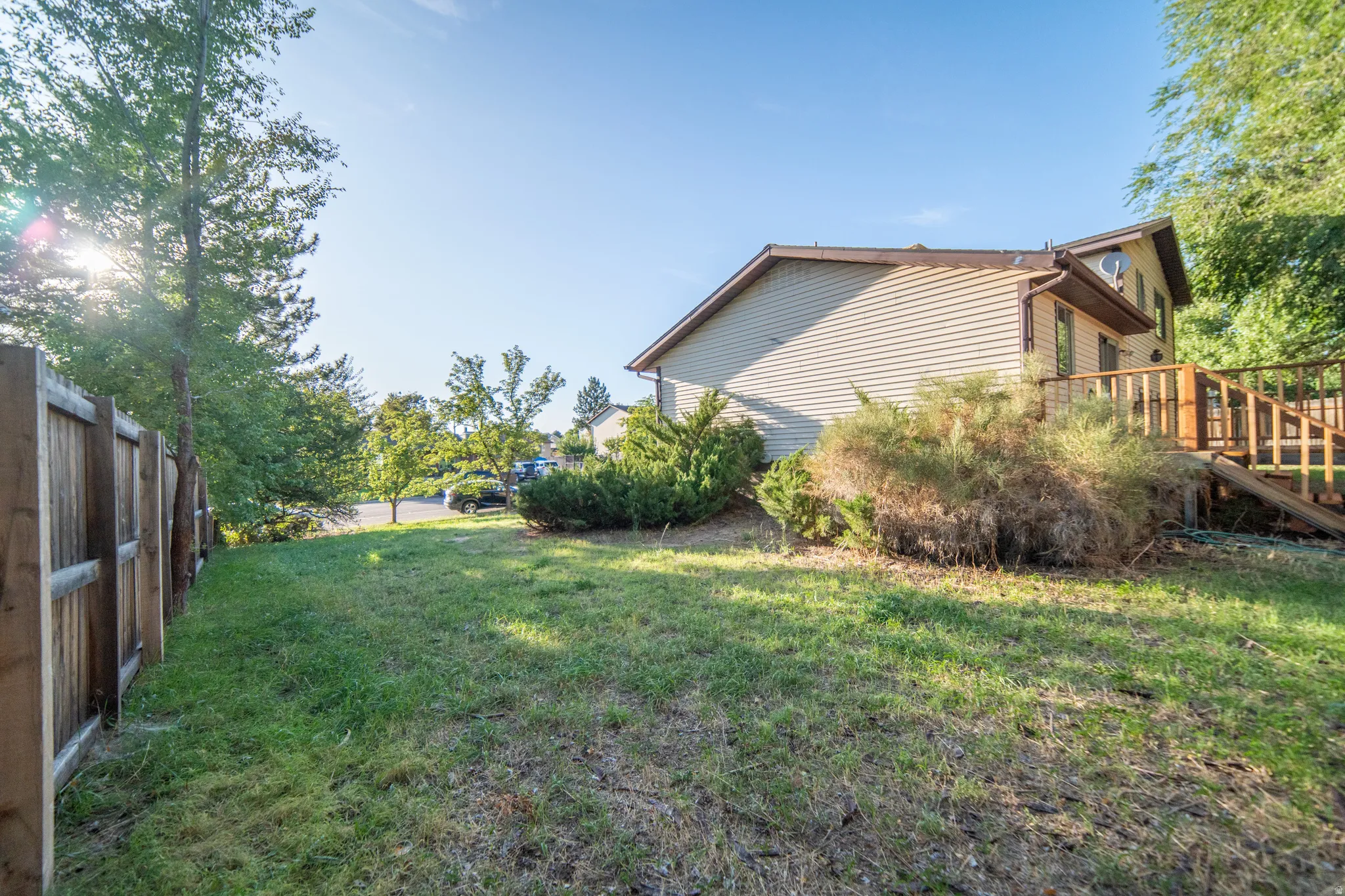 Expansive grassy yard with mature trees, wood fence, and a multi-level wood deck