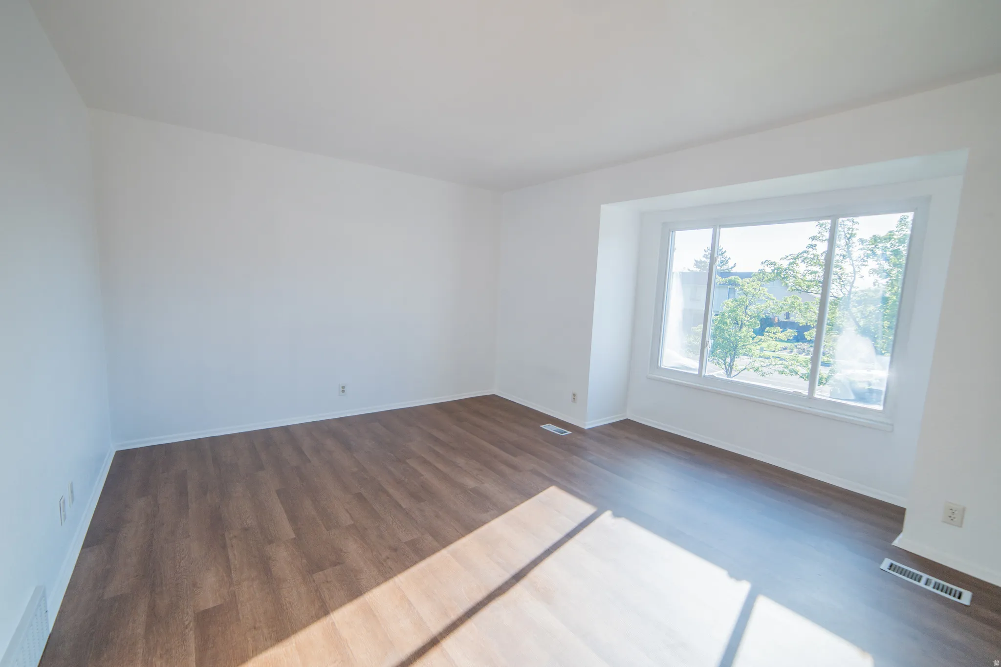 Expansive room featuring wood-finish flooring, white walls, and a large window with white trim
