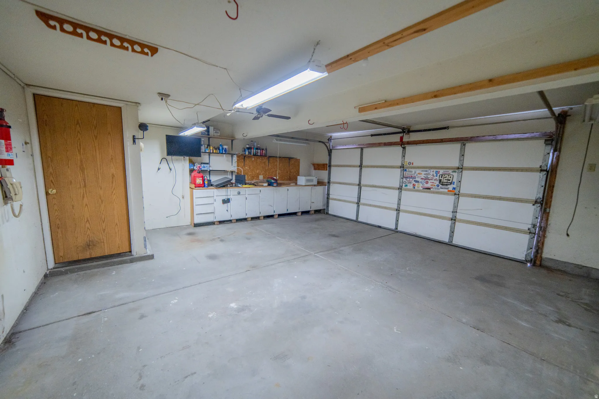 Concrete flooring, multiple storage cabinets, built-in shelving, overhead lighting, and a paneled garage door