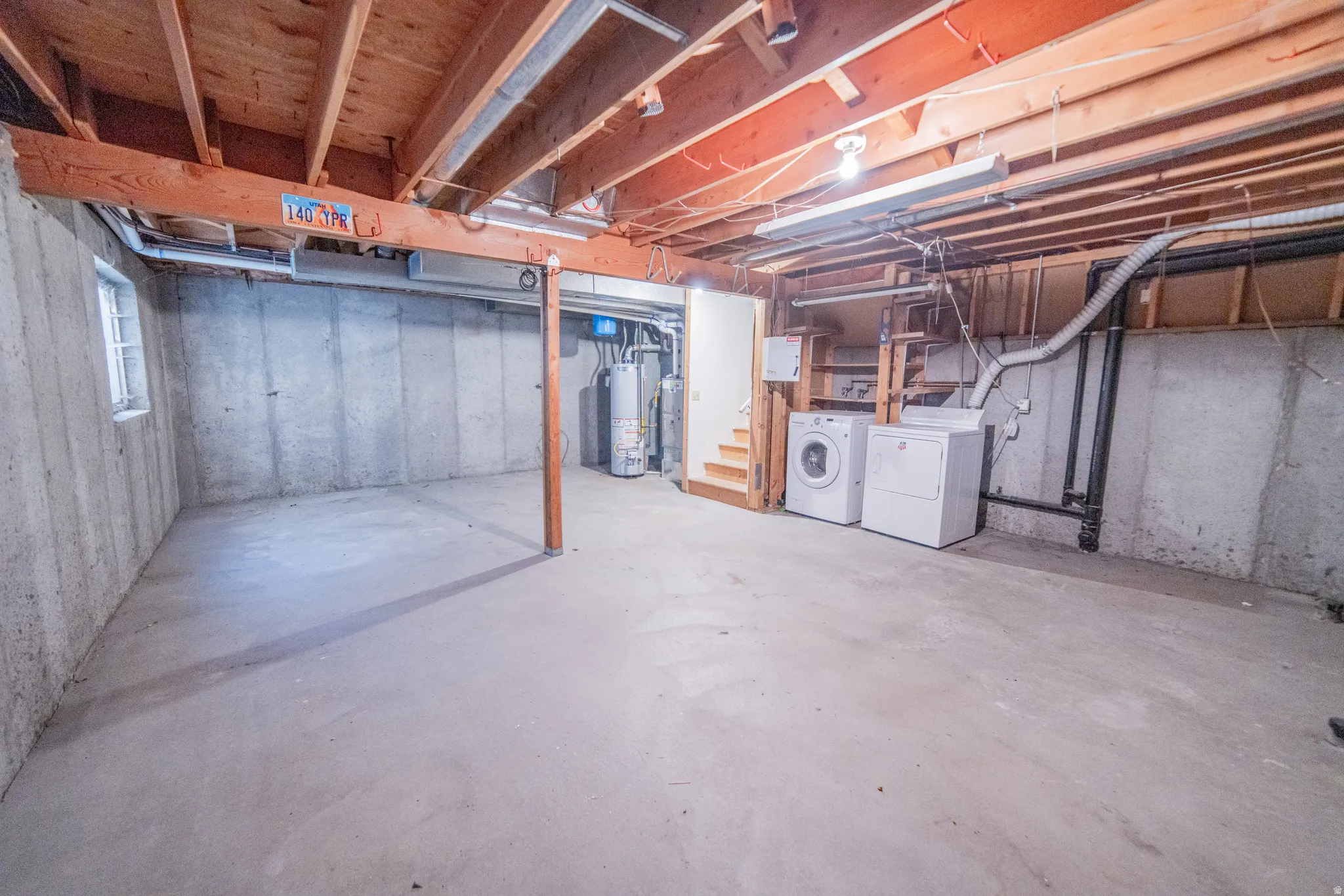 Unfinished basement with concrete flooring, exposed wood ceiling joists, and a utility area featuring a washer and dryer